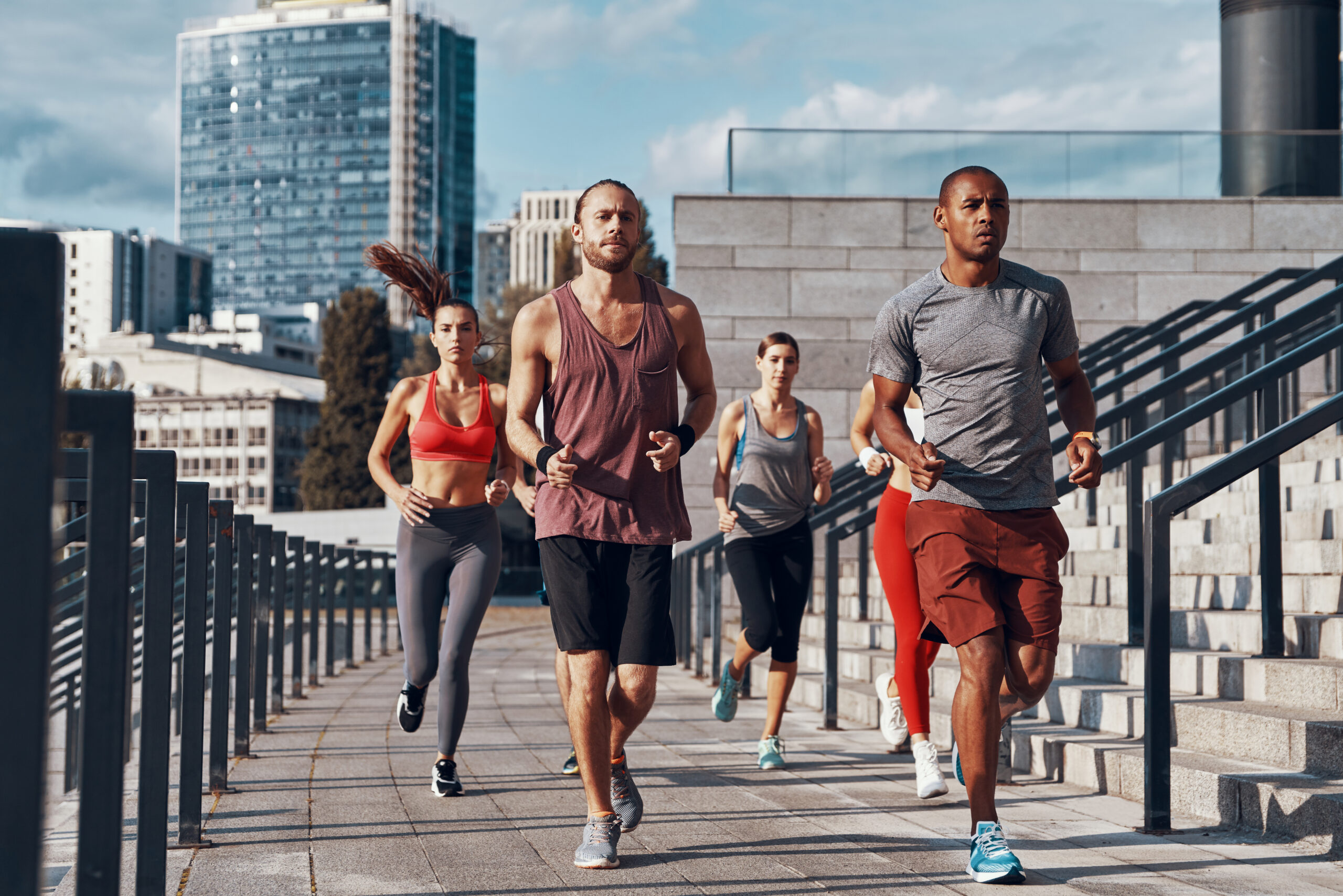 Group of five runners sprinting down an urban staircase with modern buildings in the background.
